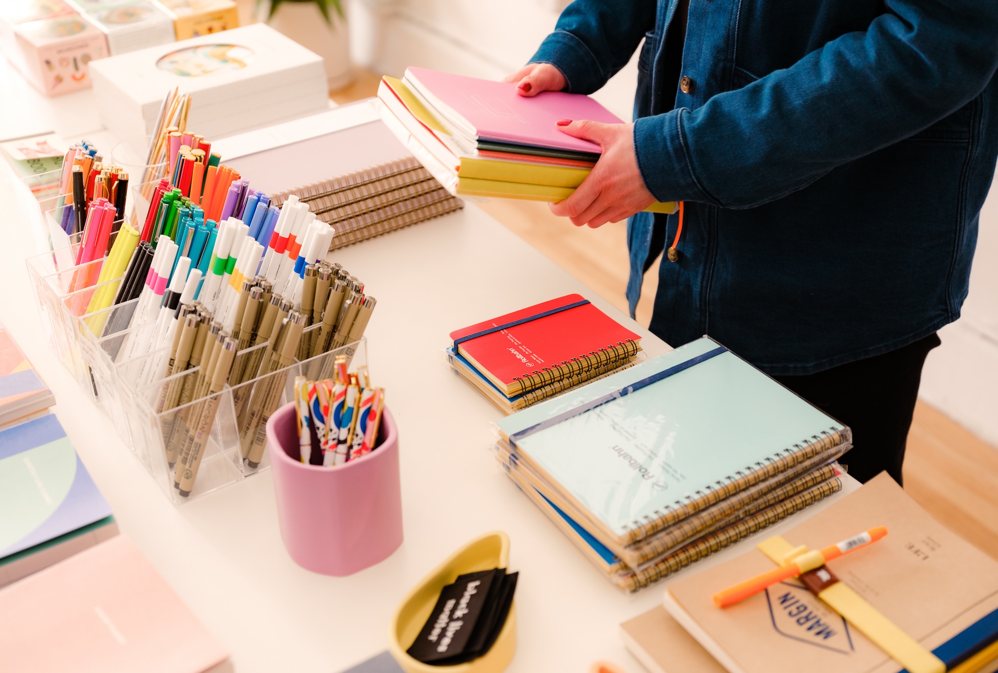 a table in an independent retail store is being stocked with brightly colored notebooks and pens