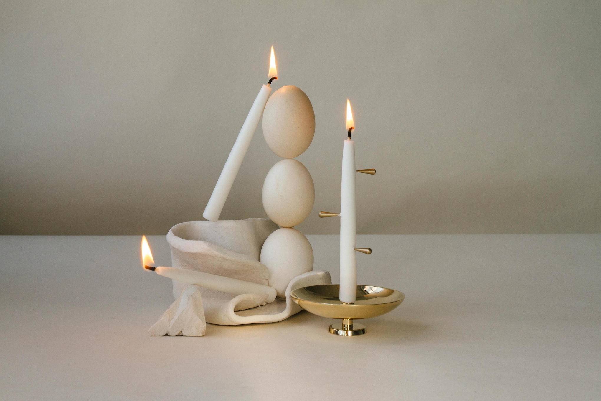 three taper candles are burning on minimalist wooden sculpture
