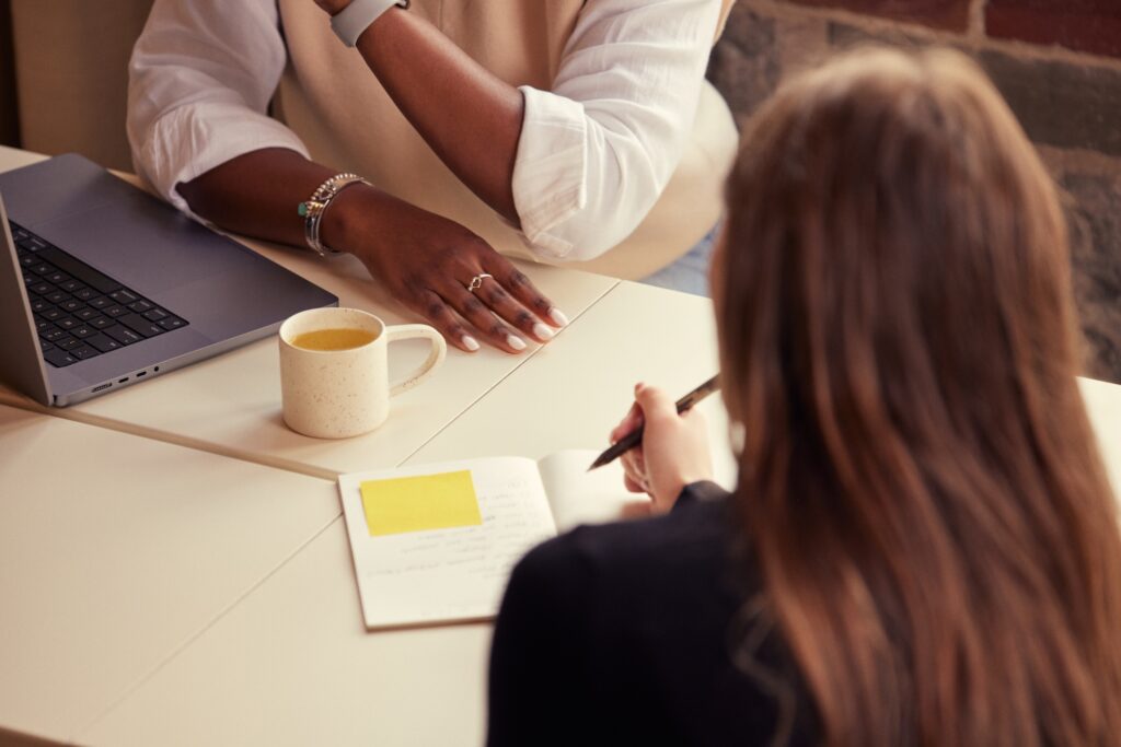 two people sit at a desk with notebooks and laptops