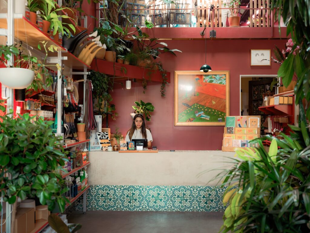 a shopkeeper stands behind the counter in a colorful, plant-filled store 