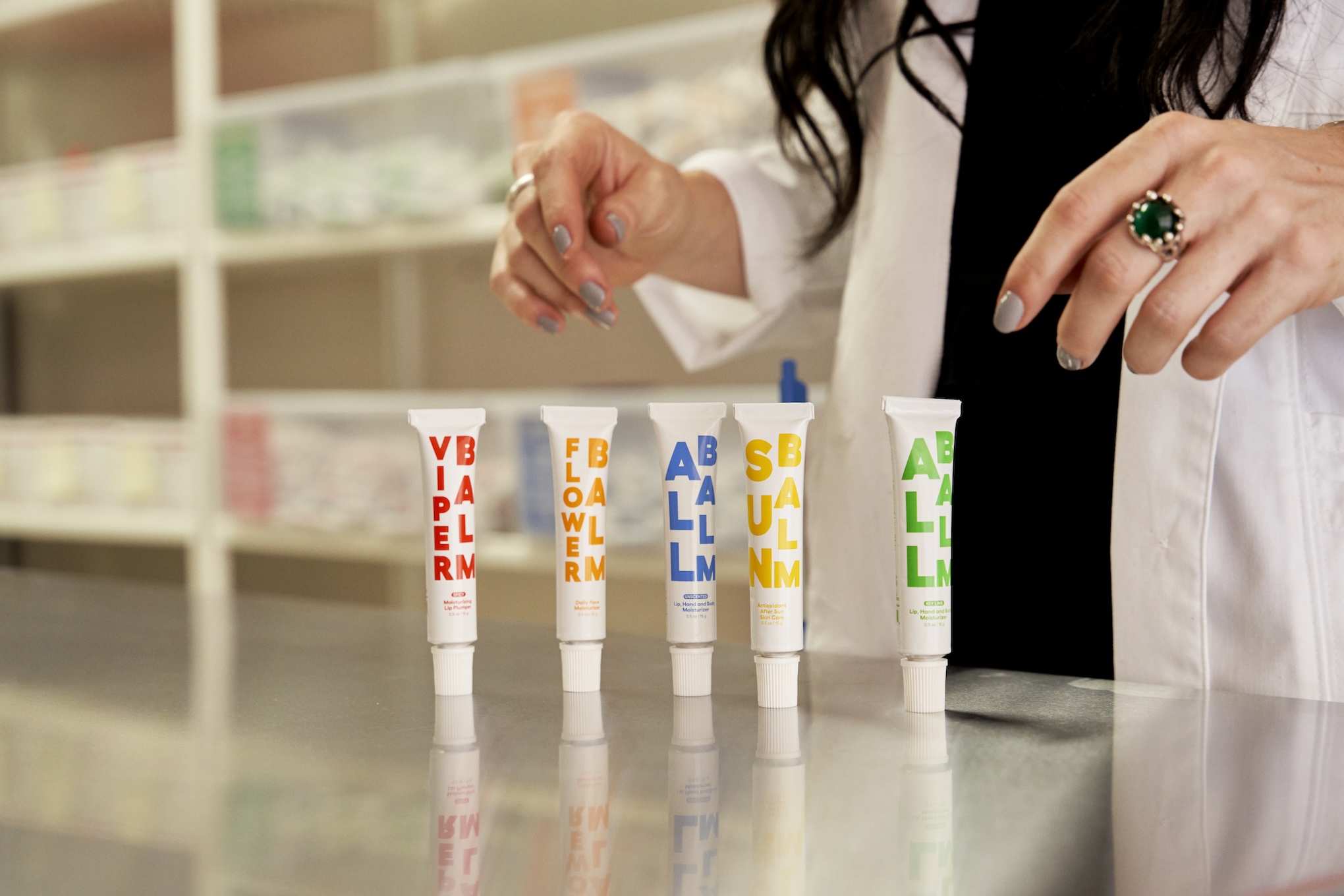 A woman's hands appear above tubes of balms with brightly colored packaging