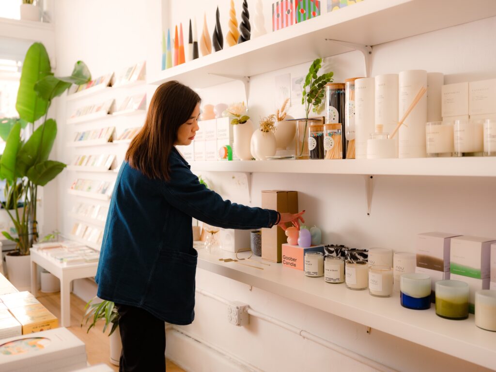 Eine frau mit lange braune Haare sucht sich eine orangene Kerze aus, nachdem sie mit Schaufenster dekorieren im Laden eingelockt wurde.