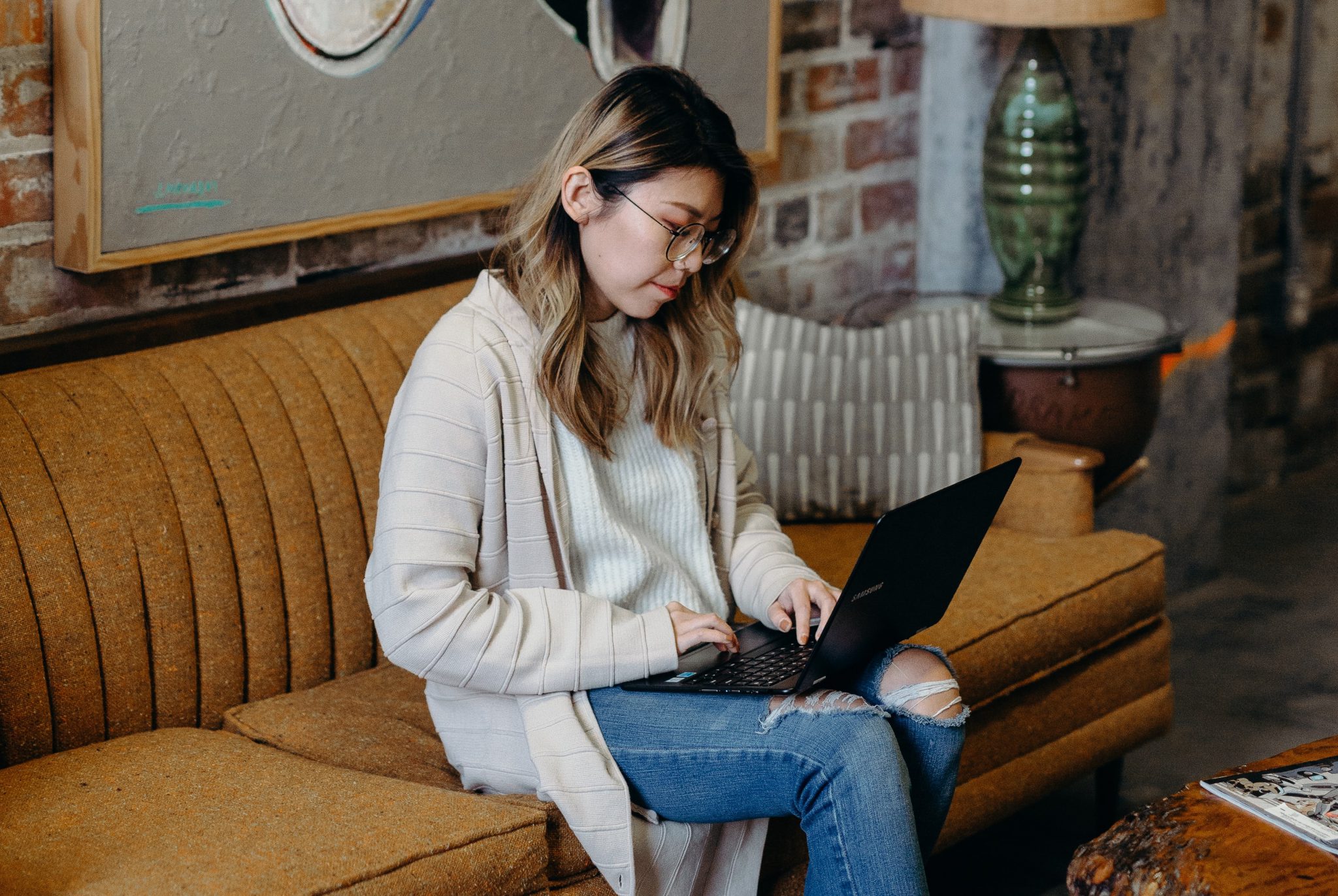 Eine Frau mit Brille sitzt auf einem Sofa und arbeitet an ihrem Laptop