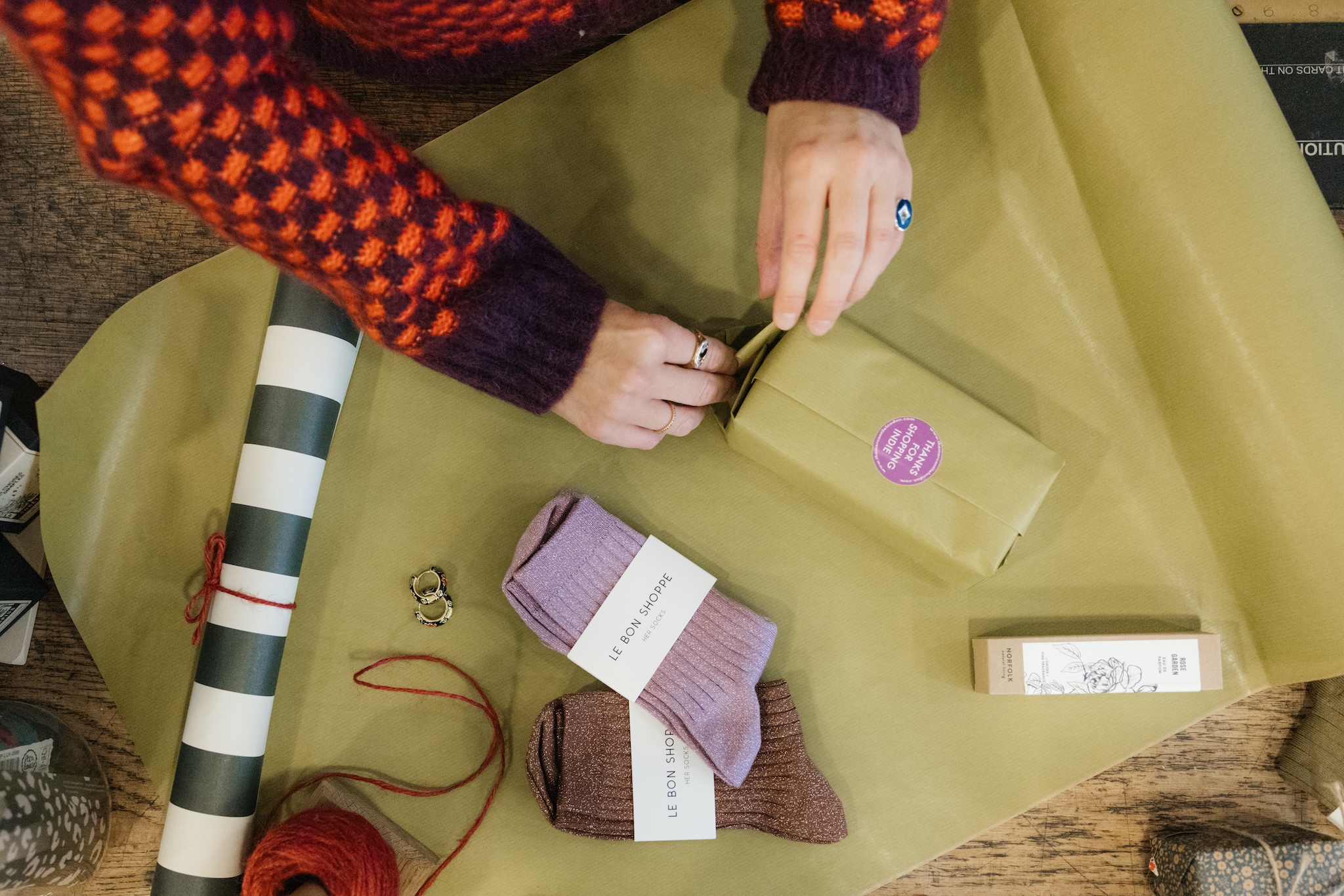 Die Hände eines Ladenbesitzers wickeln Socken und Artikel in grünes Seidenpapier ein