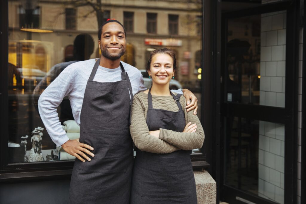 Deux commerçants souriants devant leur boutique, après avoir calculer la marge d'un produit