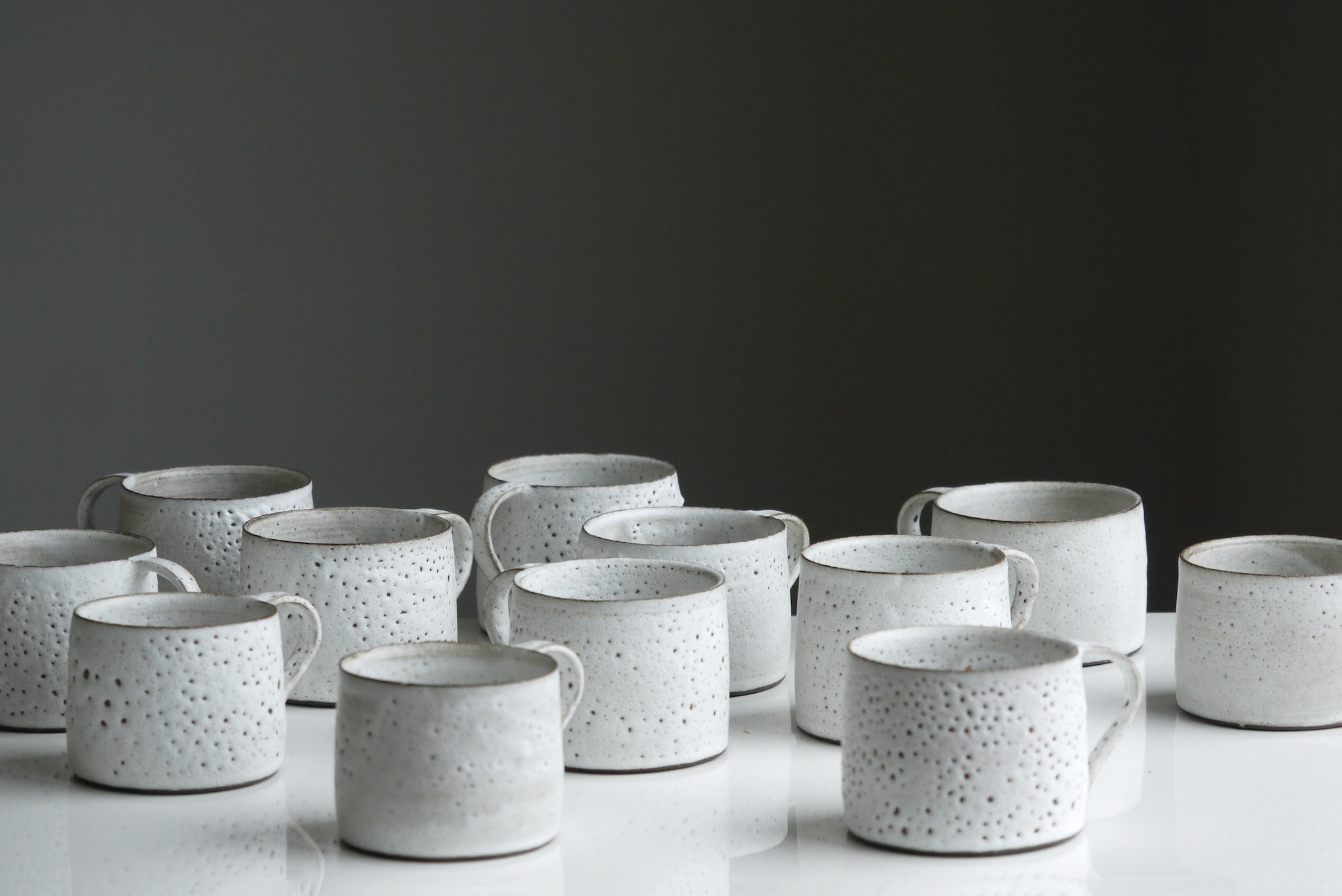 Des tasses en céramique blanche à texture trouée reposent sur une surface blanche devant un fond noir